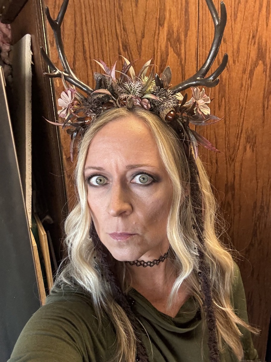Close-up of Jen in the MOSTORY floral antler headband for a forest witch costume, showing the tall dark antlers, mauve flowers, acorn beads, and beaded strands hanging beside the hair