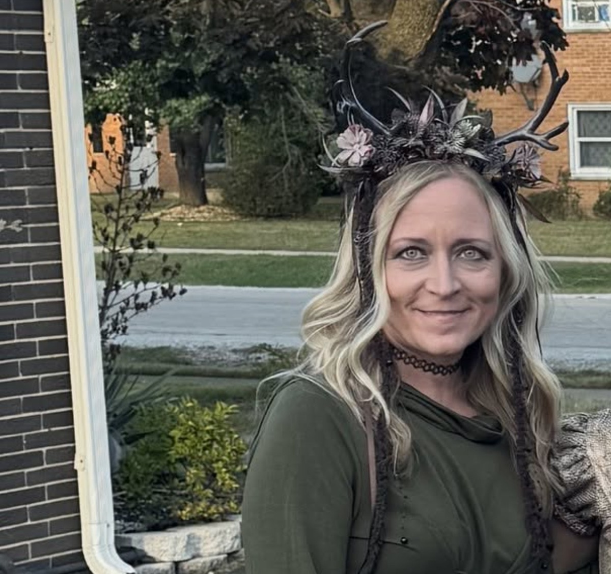 Jen wearing the MOSTORY floral antler headband outdoors at Witches Night Out with a green forest witch dress and a black choker, antlers standing tall above blonde hair