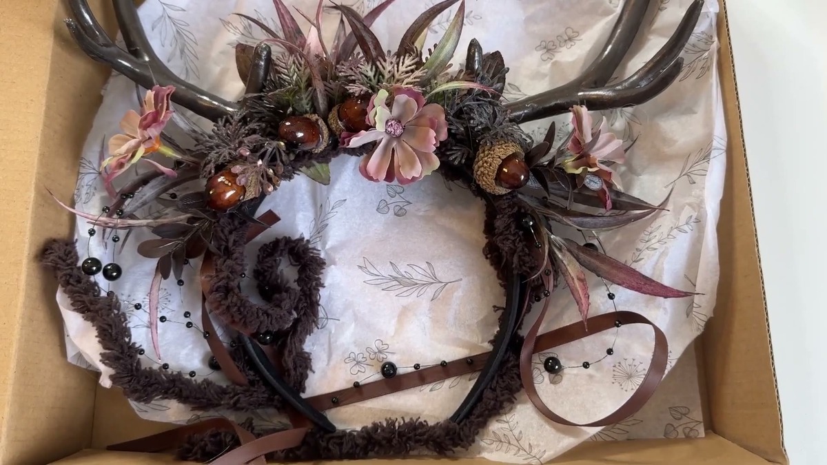 MOSTORY floral antler headband in its shipping box, dark faux antlers with mauve flowers, an acorn, moss, and beaded dangling accents