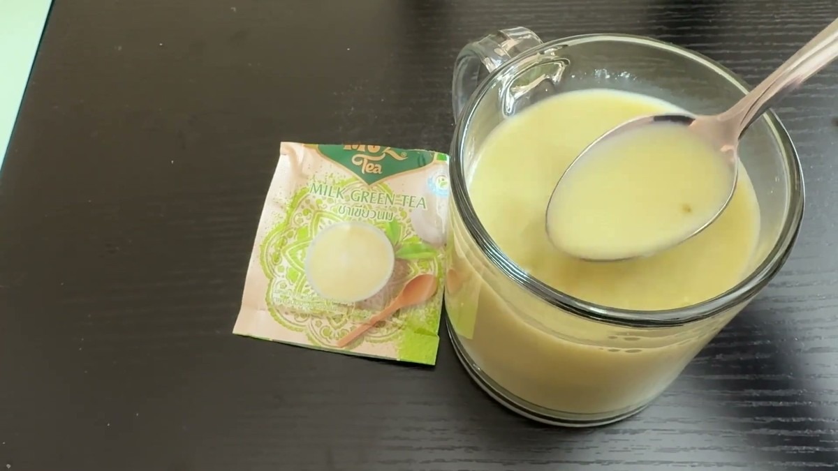 A glass mug of MUZ Tea instant milk green tea, pale and creamy, with the empty sachet on the table beside it