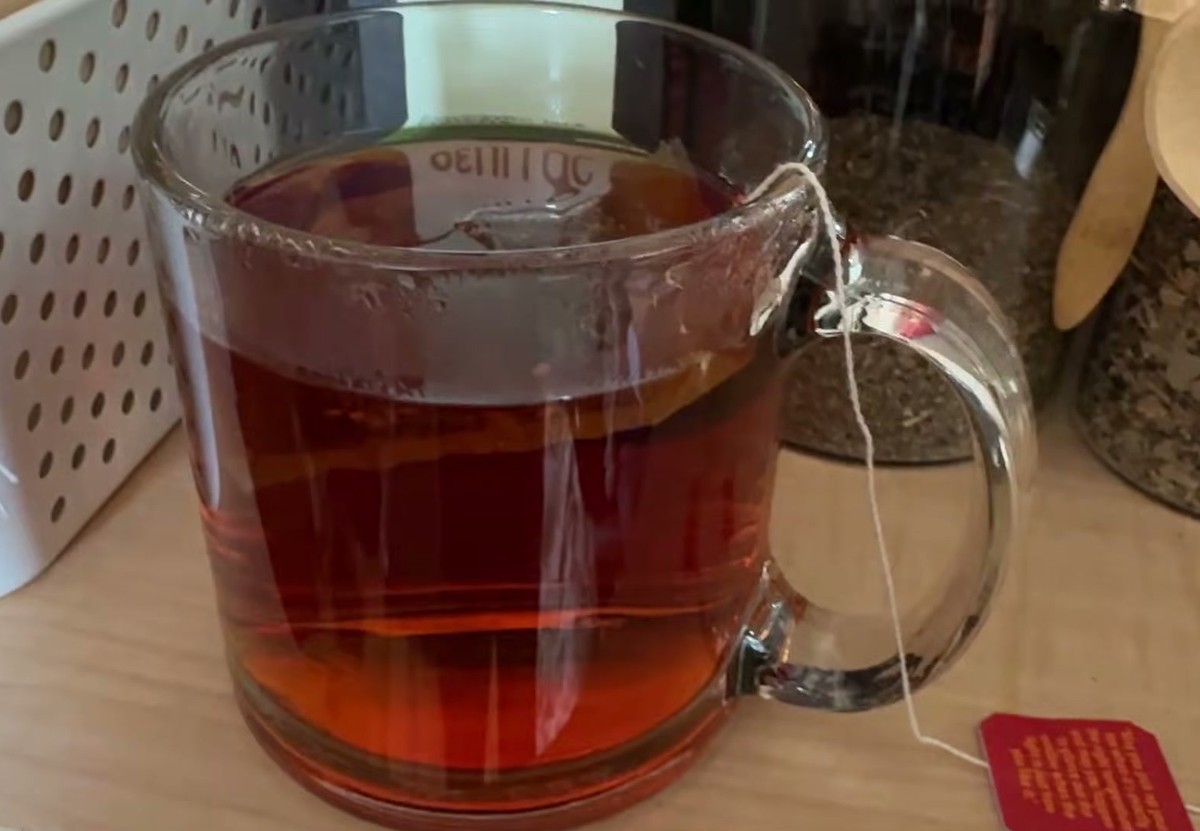 Clear glass mug of deep red brewed rooibos tea with the tea bag string and red tag hanging over the side