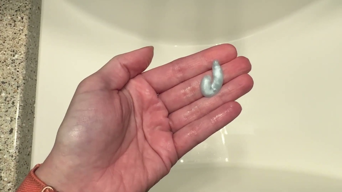 A small pump of OELY Biotin Shampoo in an open palm next to the bottle, showing the pearly white texture before lathering