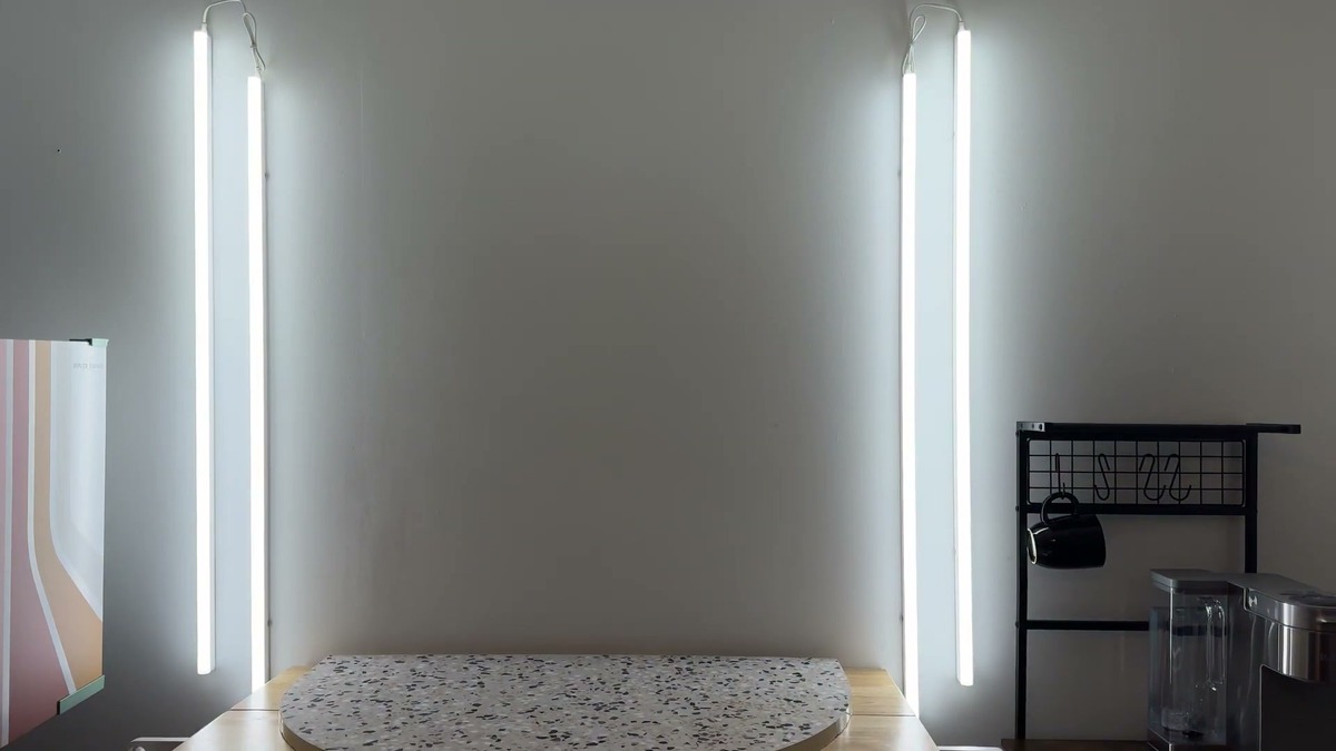 Four Pak 4FT LED shop lights mounted vertically in two linked pairs on a white office wall, switched on and lighting a terrazzo photo table