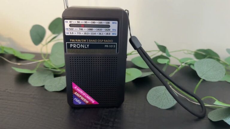 Pronly PR-1013 three band radio standing on a dark table with the telescopic antenna extended, FM AM and SW frequency dial across the front