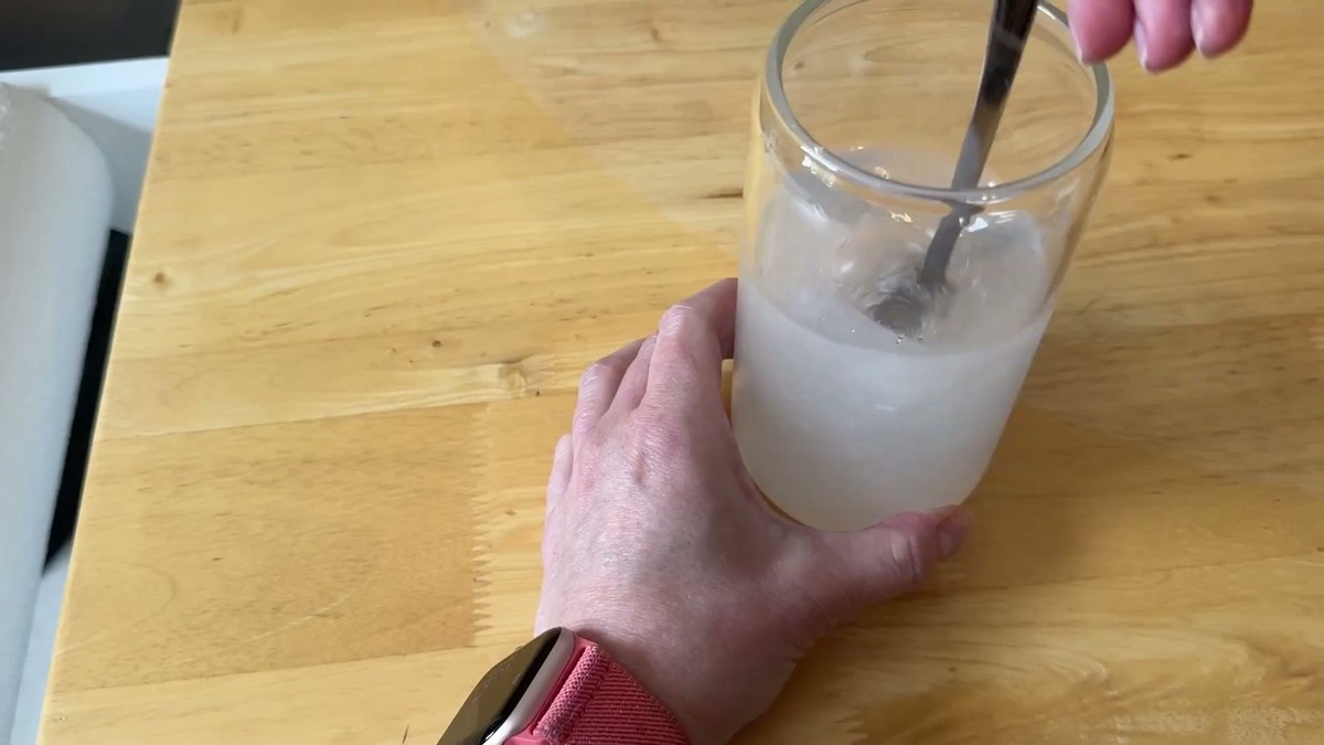 Stirring Som Sleep Calm berry powder into a glass of cold water with ice, the drink staying clear
