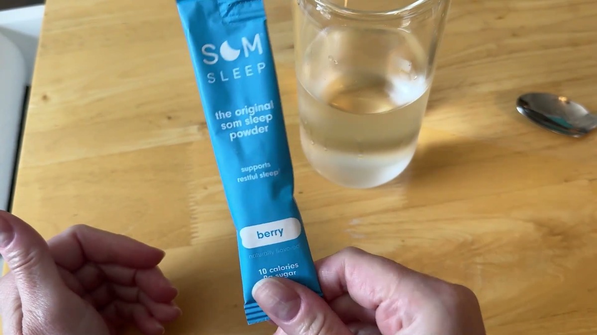 A single Som Sleep berry stick pack held next to a glass of water on a wooden table before mixing