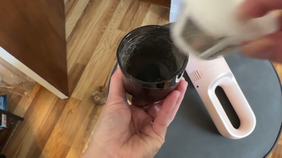 The STARUMENT vacuum's clear dust cup held up with a layer of dog fur collected inside, the pink vacuum body beside it.
