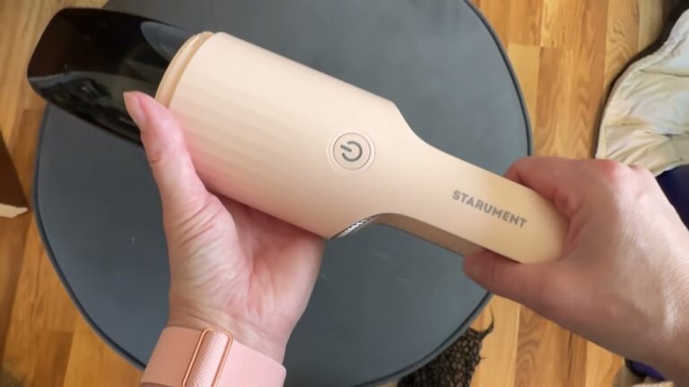 Pink STARUMENT cordless hand vacuum held horizontally in one hand, brush attachment on the nozzle and the STARUMENT name on the handle.