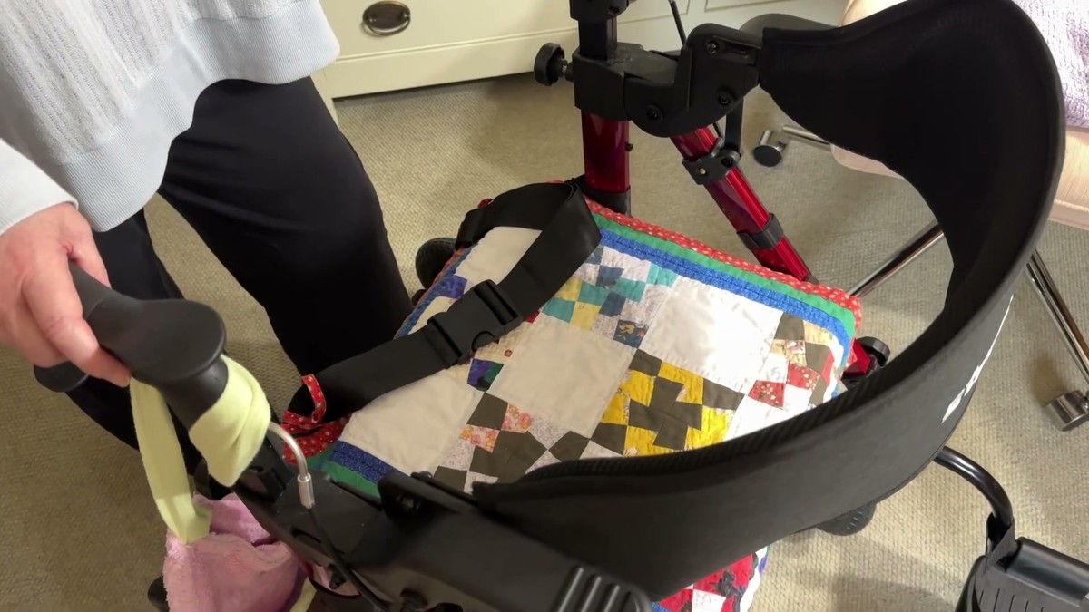 StrollAid rollator with the backrest flipped over into transport chair mode, a hand resting on the handle