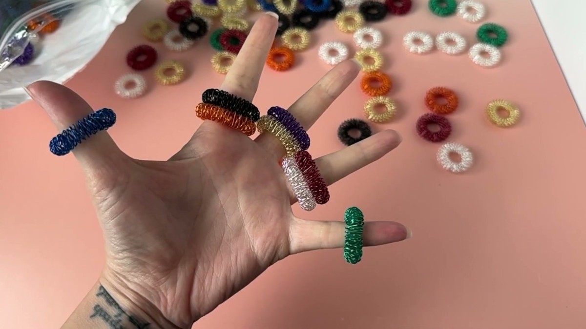 An open hand wearing several Tondiamo spiky sensory rings stacked on different fingers above a scattered pile of rings