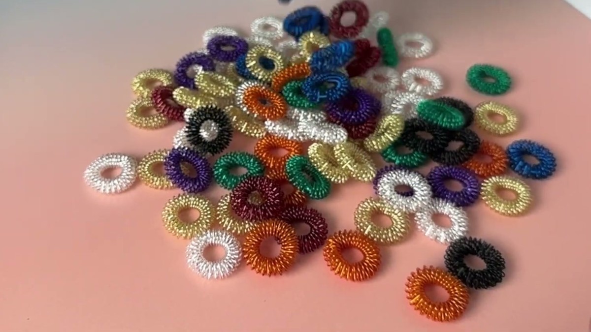 A pile of Tondiamo spiky sensory finger rings in gold, silver, orange, green, blue, purple, red and black on a pink desk