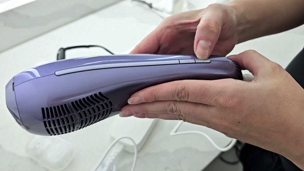 Side view of the Ulike Air 10 IPL device held in two hands showing the cooling vents at the back and the mode buttons on top
