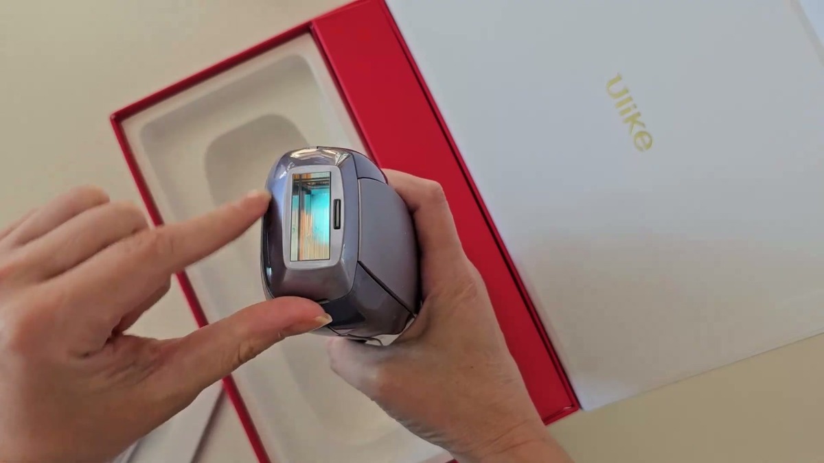 Hands holding the Ulike Air 10 IPL device head-on to show the sapphire treatment window and skin sensor above the open box