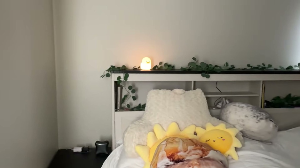 UNEEDE Benson duck night light glowing on a bedroom shelf above a bed with pillows and a plush toy, showing how soft the light is across the room