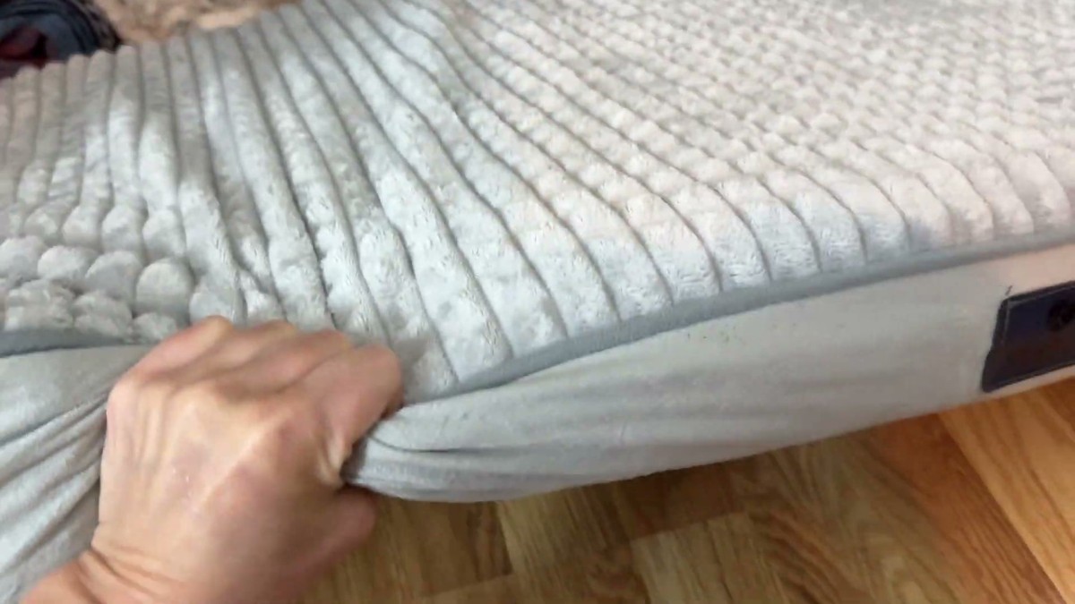 A hand pinching the soft ribbed flannel cover on the edge of the Veehoo orthopedic dog bed to show its thickness
