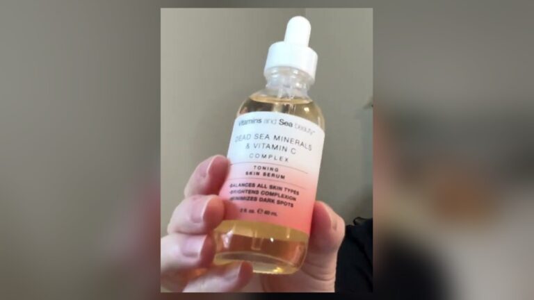 A hand holding a 2 oz glass dropper bottle of Vitamins and Sea Beauty Dead Sea Minerals and Vitamin C Complex toning skin serum with a white and coral label