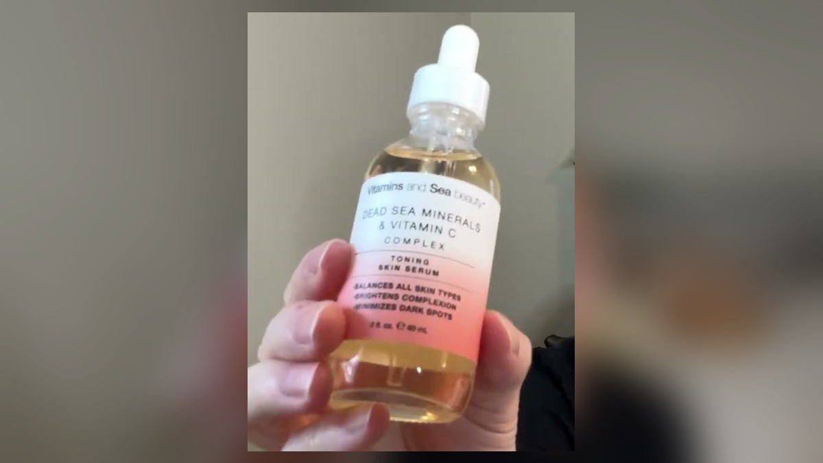 A hand holding a 2 oz glass dropper bottle of Vitamins and Sea Beauty Dead Sea Minerals and Vitamin C Complex toning skin serum with a white and coral label