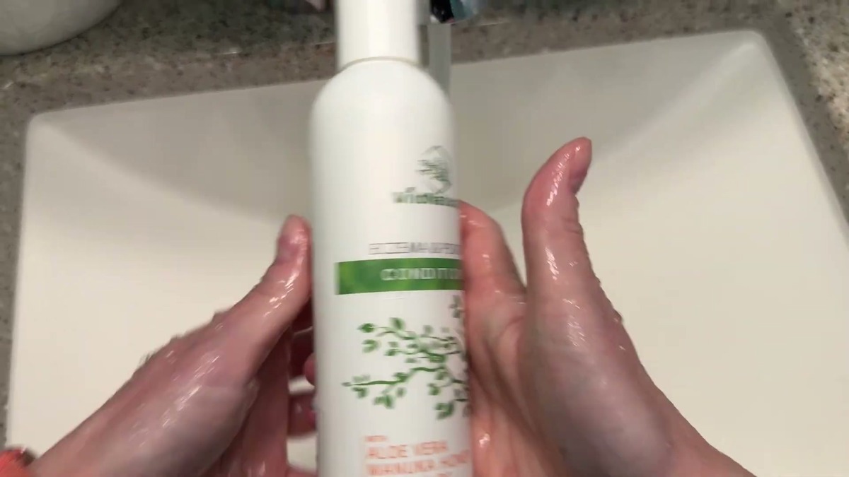 Wild Naturals eczema conditioner bottle held over a bathroom sink with wet hands