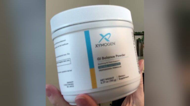 XYMOGEN GI Balance Powder in natural chai flavor, a white 6.77 oz tub with a blue and gold label, held up in one hand