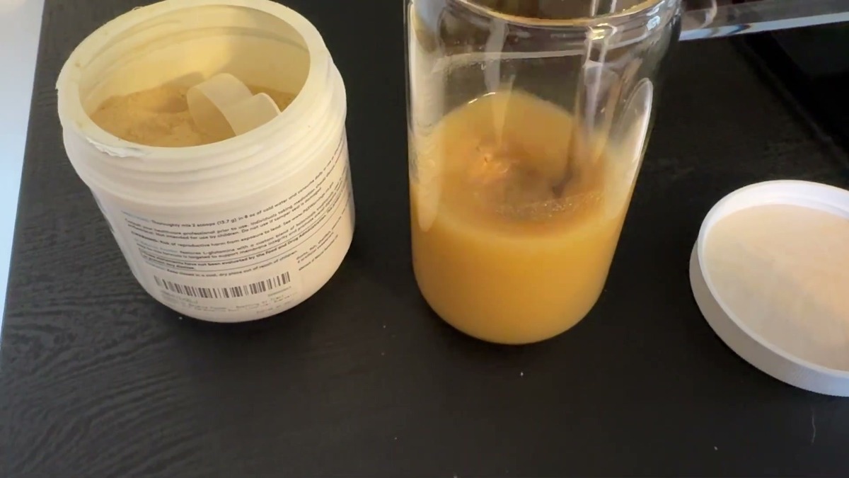 XYMOGEN GI Balance chai powder stirred into a glass of water, next to the open tub with its scoop inside