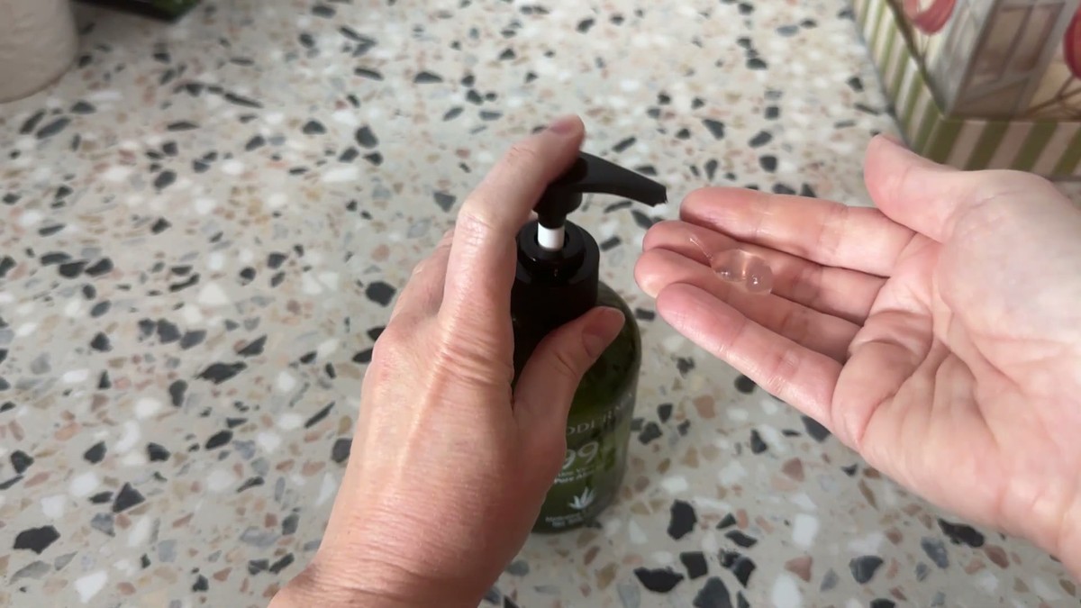 Hand pumping a clear blob of Aloderma aloe vera gel into an open palm next to the green bottle