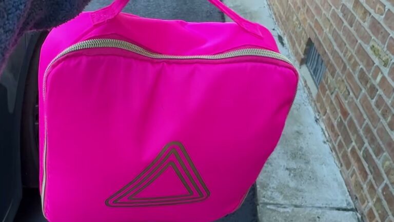 BLINGSTING car emergency kit in its hot pink zip case with a gold triangle on the front, held up by the handle beside a car