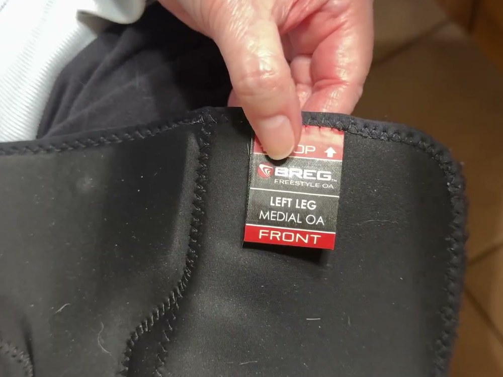 Inside tag of the Breg Freestyle OA knee brace reading Top, Left Leg, Medial OA, Front, held up on the neoprene liner