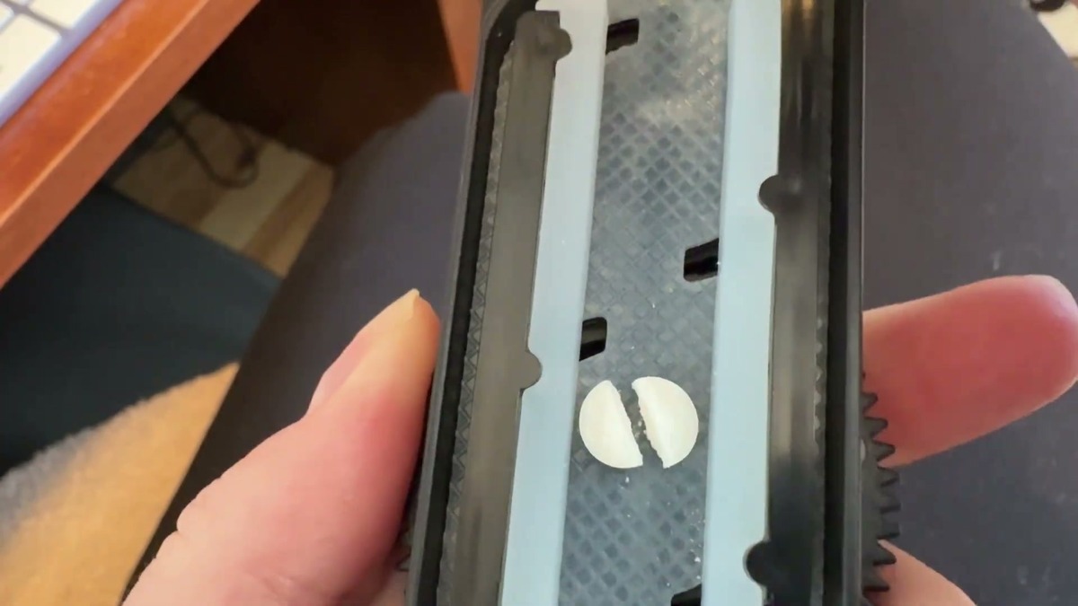 A round white scored pill split in two inside the DEPAD pill cutter, with the cut sitting just beside the score line