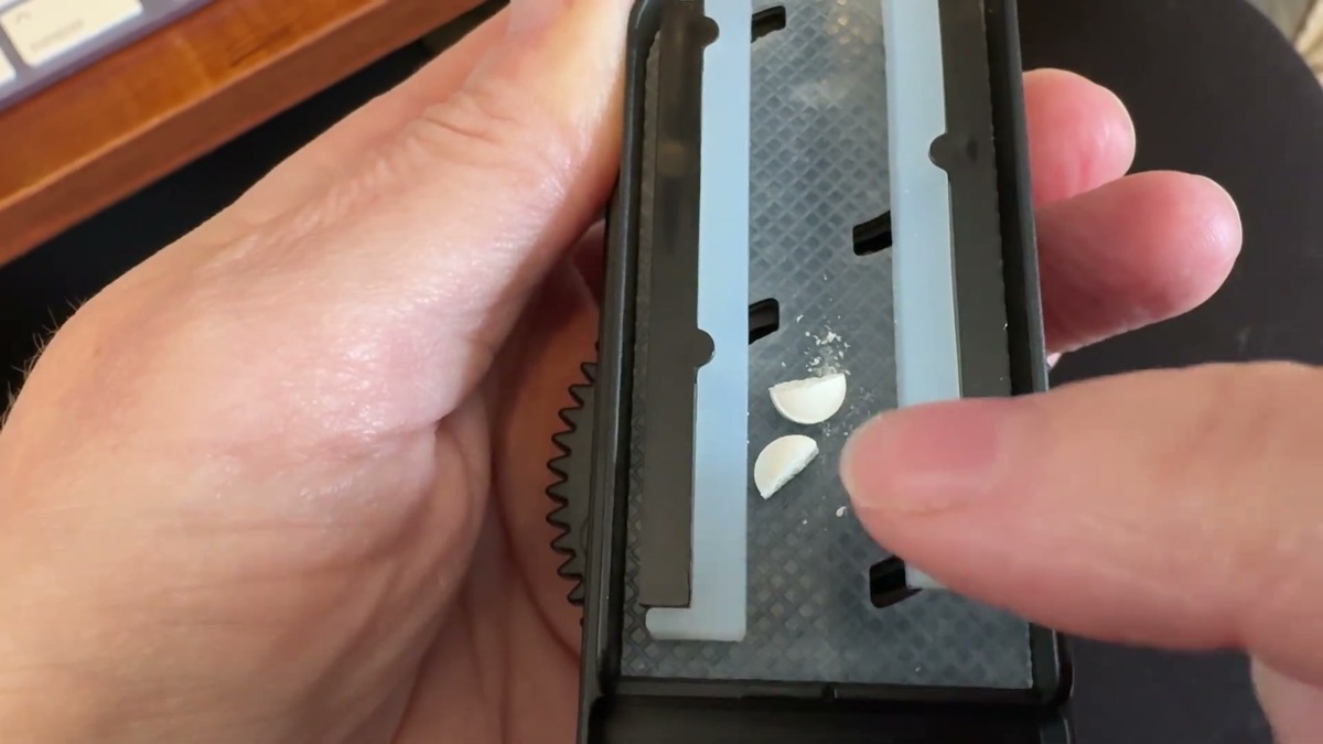 A tiny white pill cut into two halves between the silicone bars of the DEPAD pill cutter