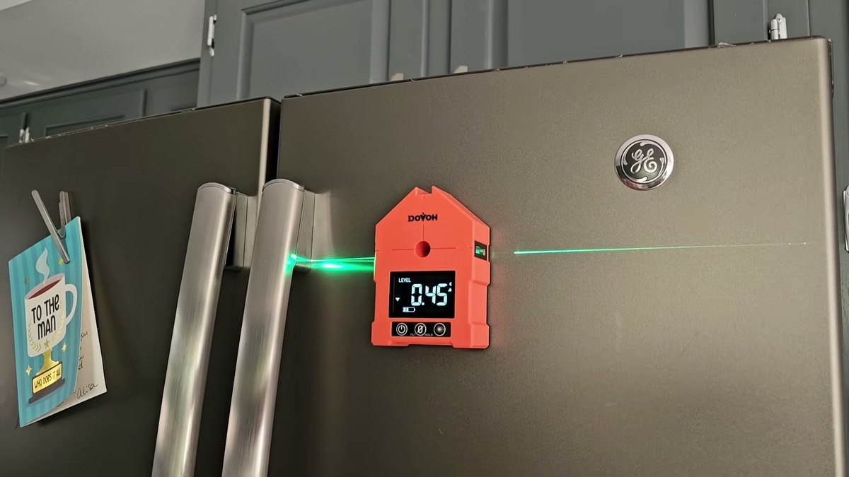 DOVOH WG-3L digital angle finder stuck to a refrigerator door by its magnet, reading 0.45 degrees with green laser lines running left and right