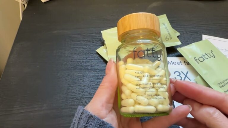 Fatty15 glass jar with a wooden lid, filled with small cream-colored capsules, held above the green refill pouches