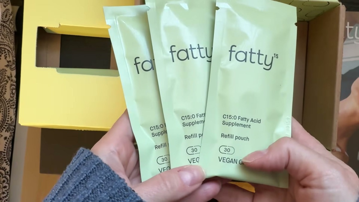 Three green Fatty15 C15:0 fatty acid supplement refill pouches fanned out over the shipping box, each marked 30 vegan capsules