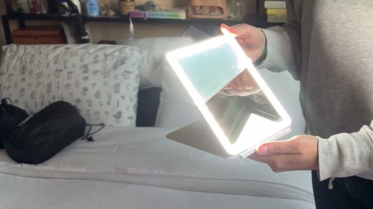 FUNTOUCH rechargeable travel makeup mirror glowing with its ring of LED lights, held open on its fold-out stand over a bed