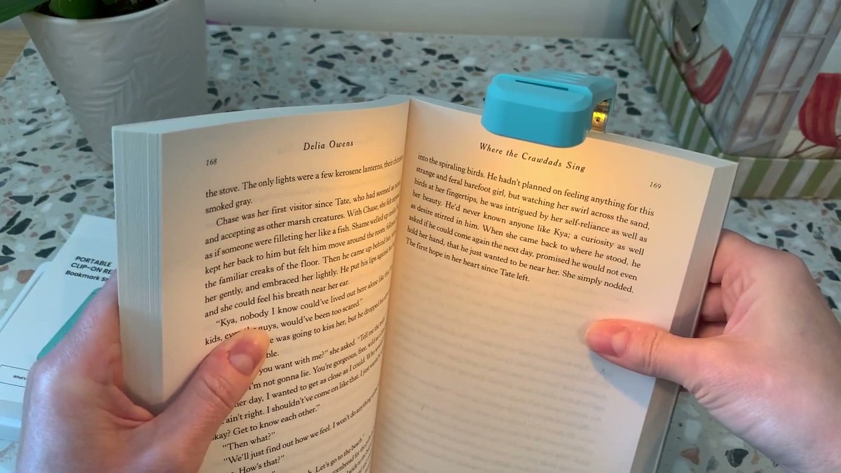 Glocusent book light clipped to the top of an open paperback, casting warm amber light across the page