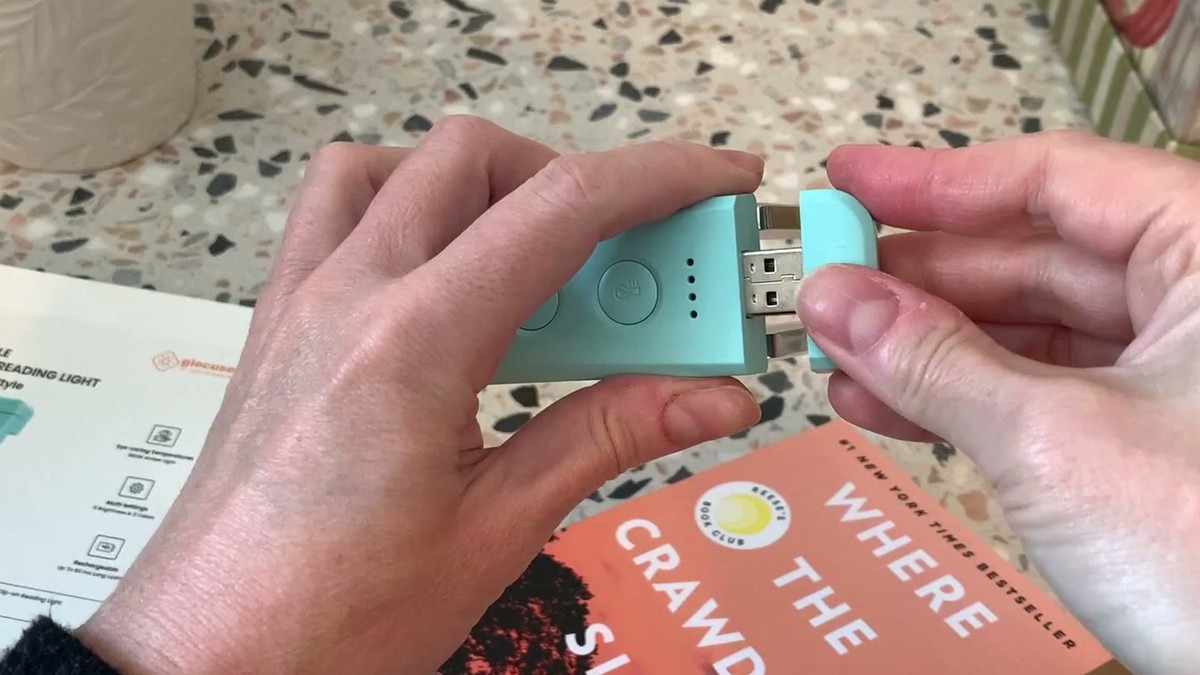 Hands pulling the end cap off the teal Glocusent book light to show its built-in USB-A charging plug