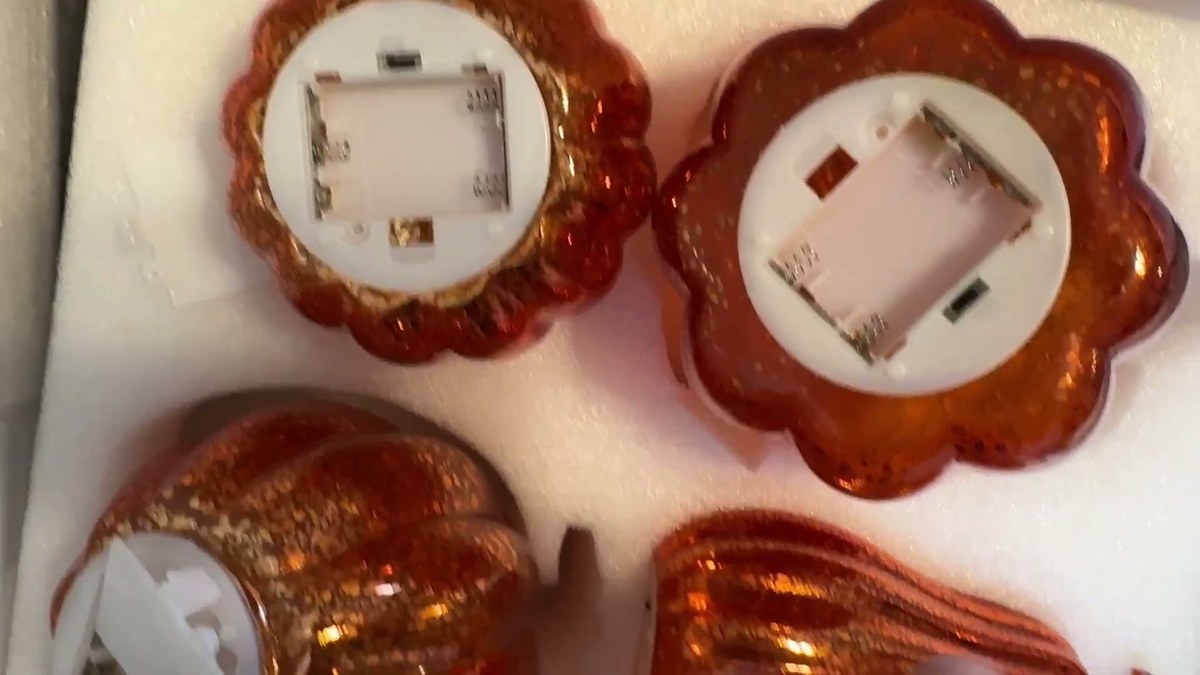 Bottoms of two Glooglitter glass pumpkins showing the white battery compartments, with two more pumpkins in the foam tray below