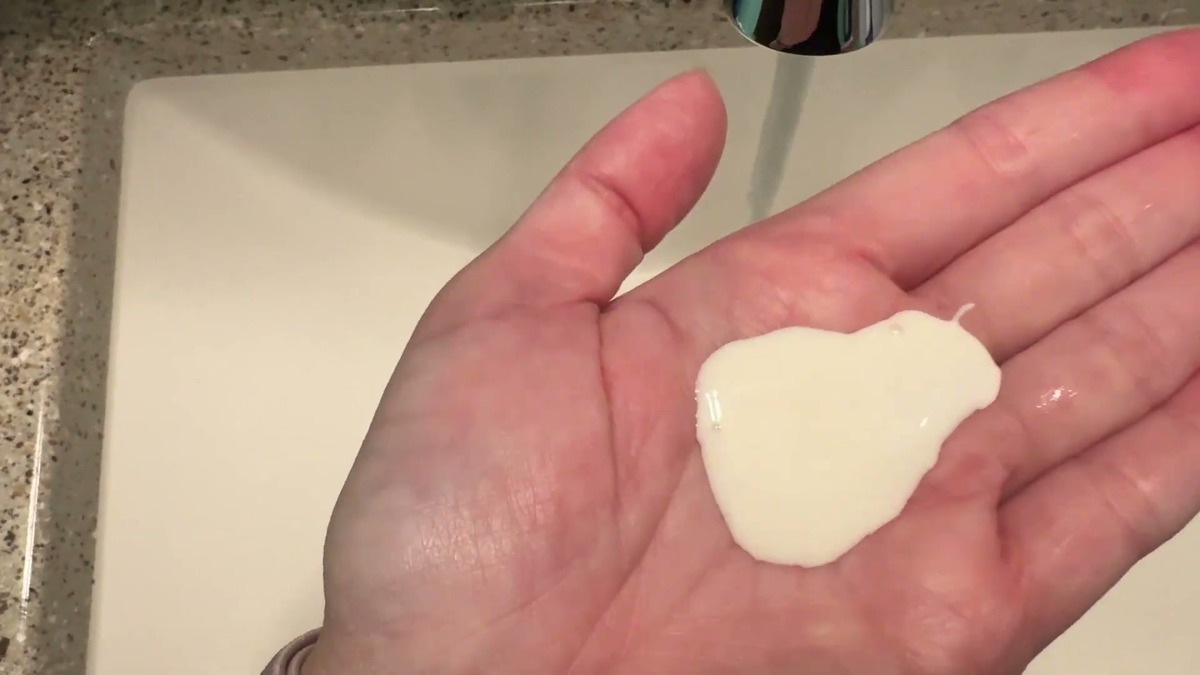A pump of Hermon Medicated Shampoo sitting in an open palm over a bathroom sink, thick and off-white like lotion