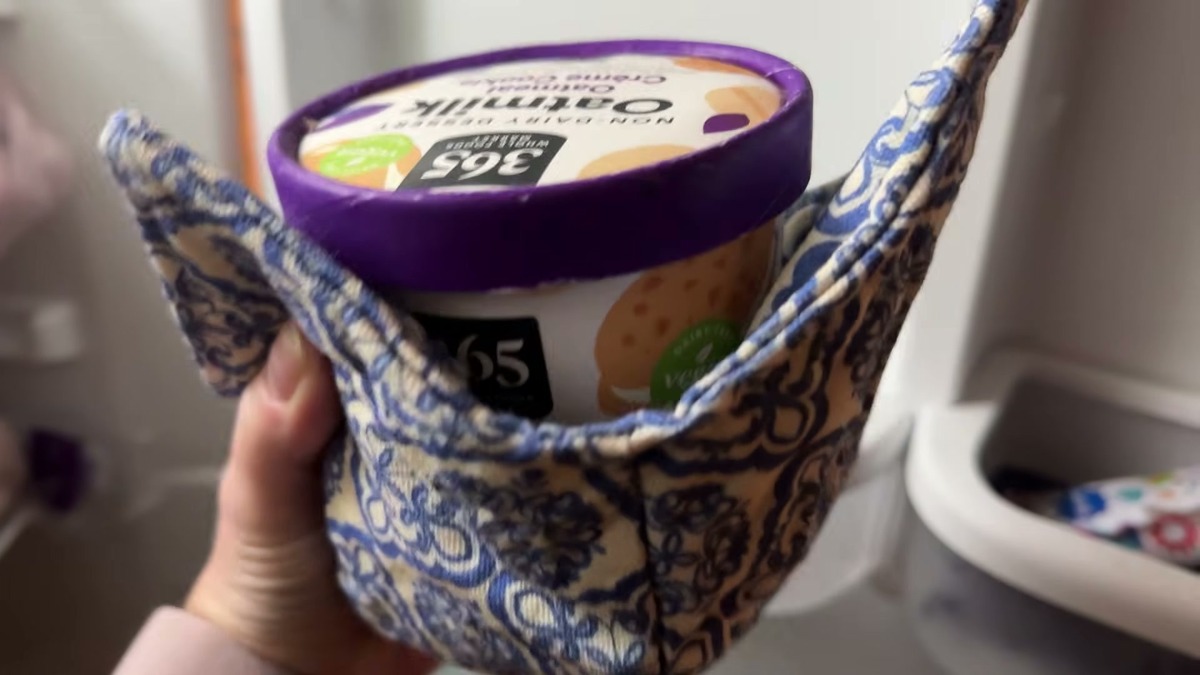 A pint of oat milk frozen dessert tucked into a blue and white patterned JounLoin bowl cozy held in one hand
