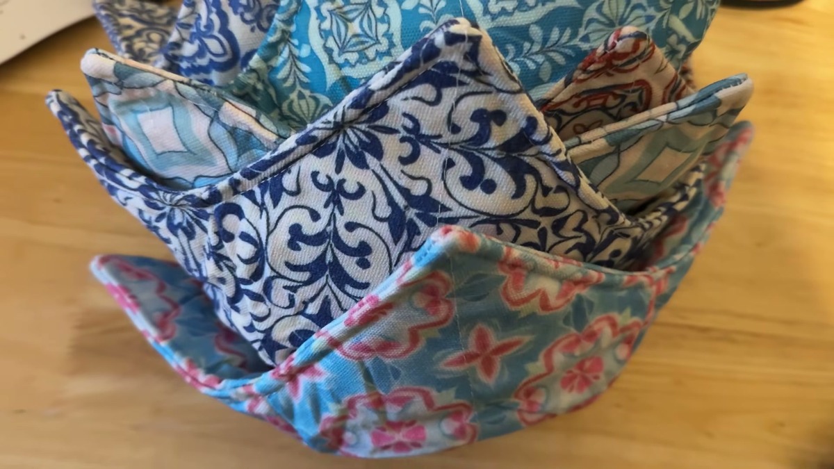 Several JounLoin cotton bowl cozies in blue, teal and pink patterns nested inside each other on a wooden table