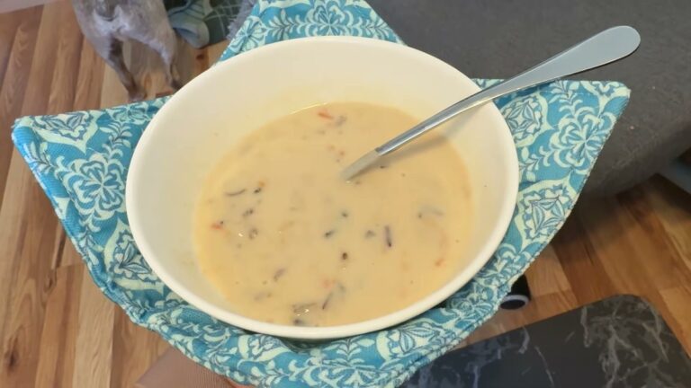A white bowl of creamy soup with a spoon sitting in a teal patterned JounLoin cotton bowl cozy, held over a wood floor
