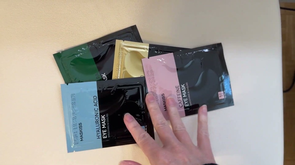 Four individually sealed Maskiss eye patch packets in green aloe vera, gold 24K, pink caffeine and blue hyaluronic acid on a white table