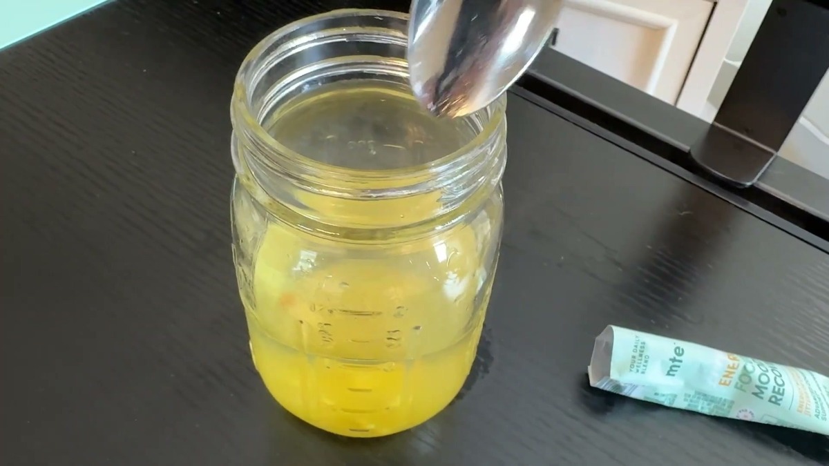 Glass jar of bright yellow mandarin orange MTE energy drink being stirred with a spoon next to an open MTE stick pack