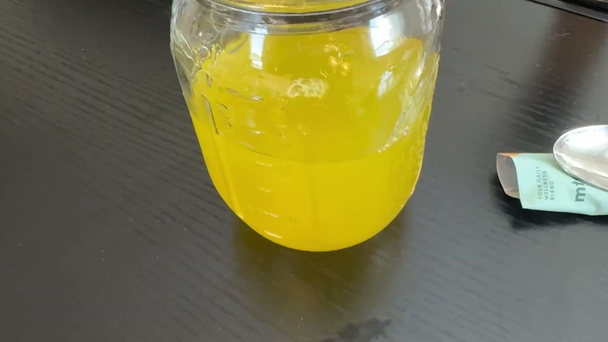 Close view of a jar filled with mixed MTE mandarin orange energy drink beside a spoon and MTE stick packs on a dark table