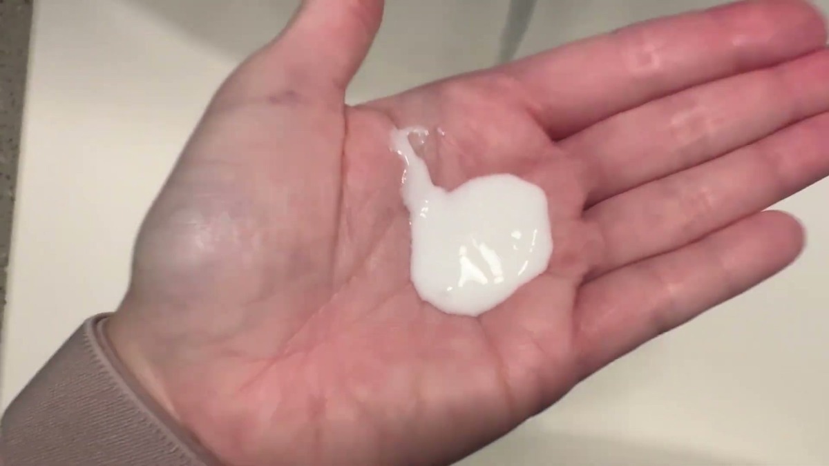 A dollop of white ProBliva shampoo sitting in an open palm over a bathroom sink