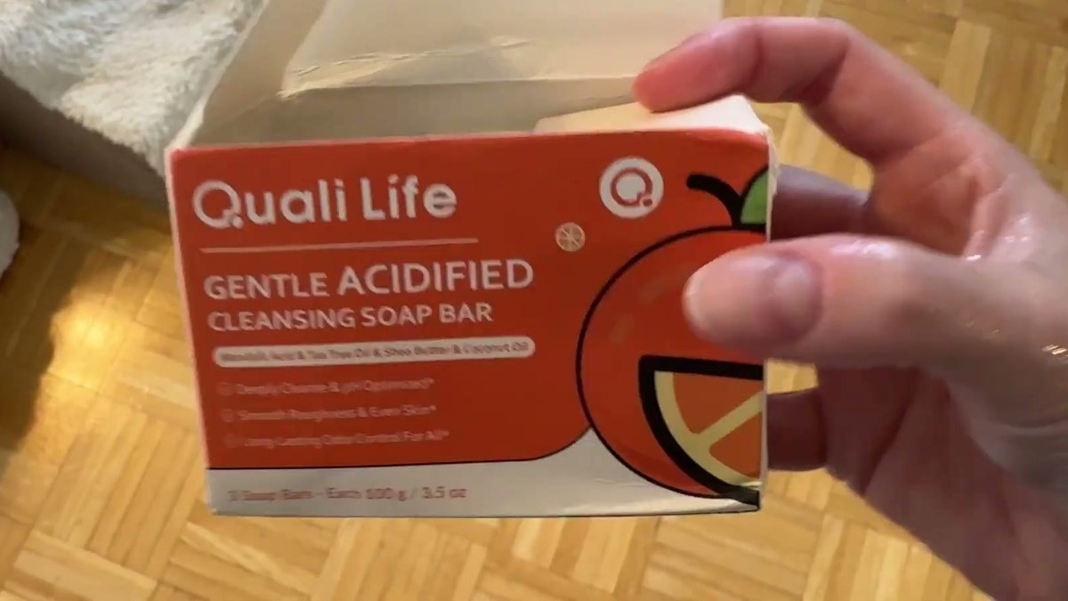 Hand holding the orange Quali Life Gentle Acidified Cleansing Soap Bar box with a tangerine graphic, opened at the top