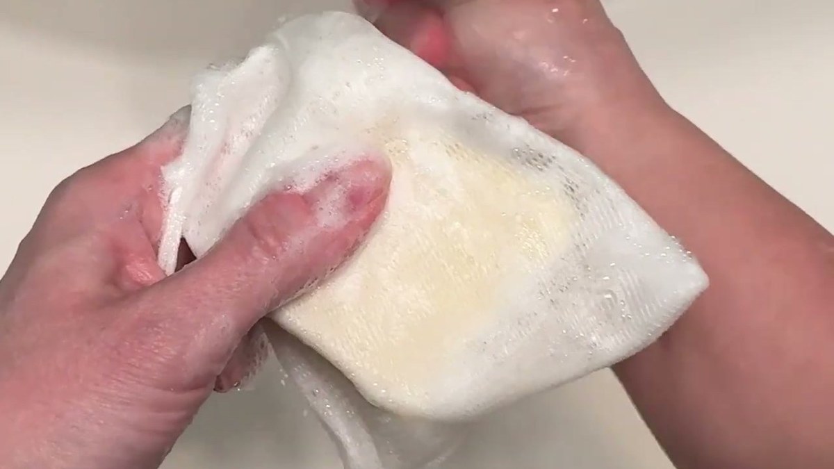 Quali Life soap bar inside its white mesh soap bag, foamy with lather under a running faucet