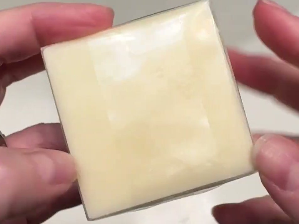 Pale yellow square Quali Life acidified soap bar still in its clear wrap, held over a bathroom sink