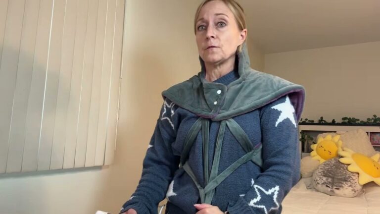 Jen wearing the gray reliefRX Snug-Fit heating pad, with the high neck panel snapped up her neck and the straps crossing her chest over a blue star sweater