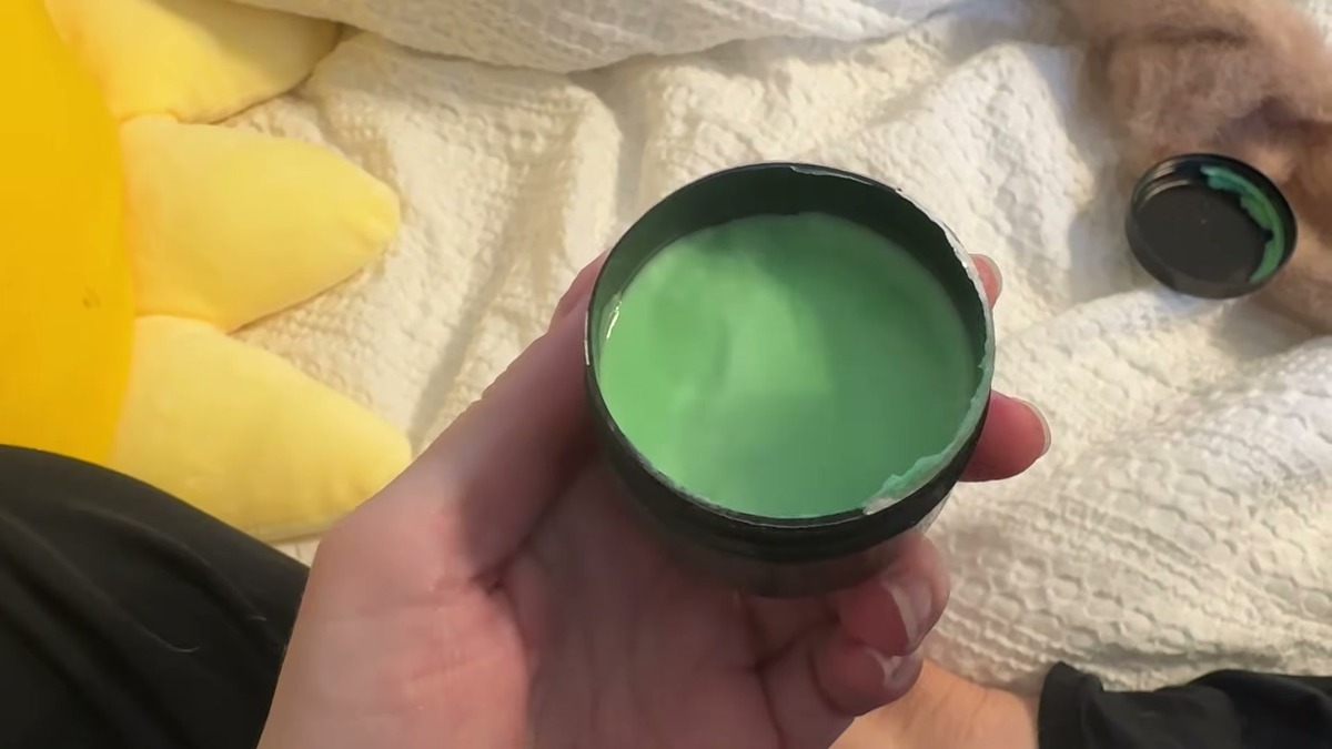 Open jar of Rozino foot cream held over a white blanket, showing the bright green cream inside