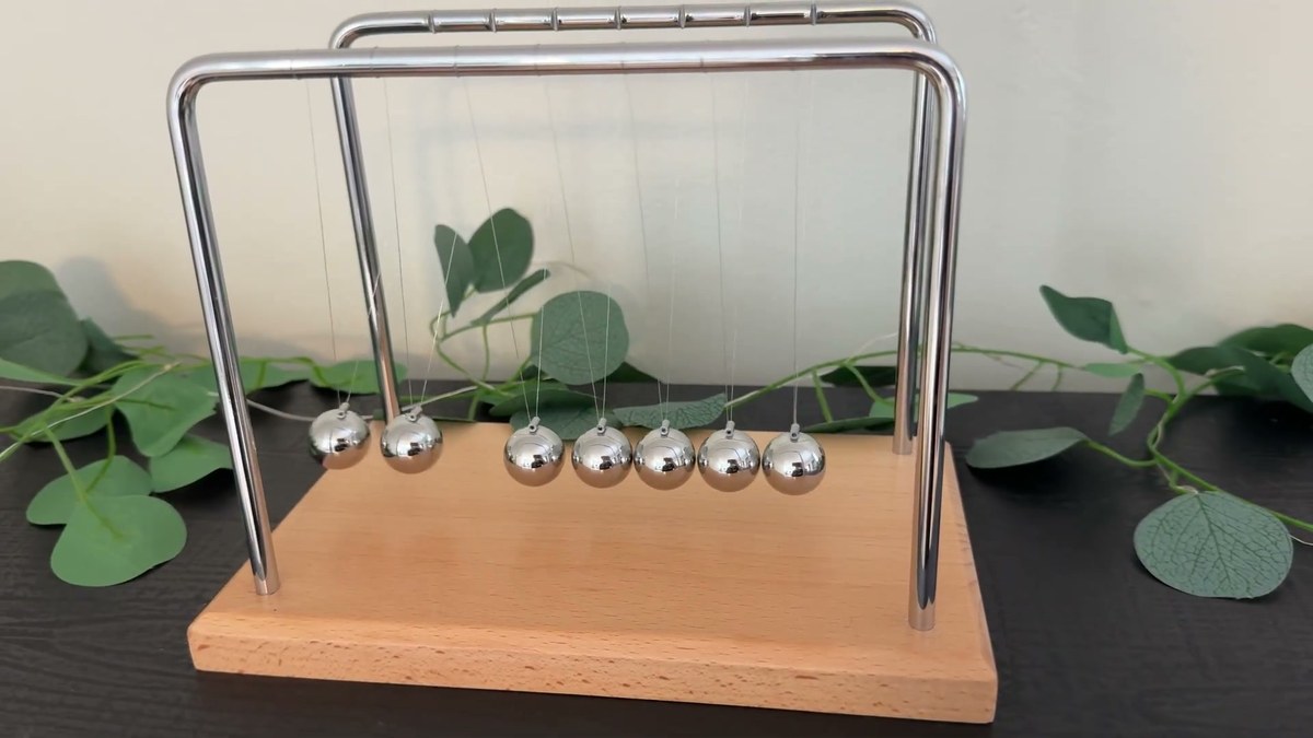 Two chrome balls swinging out from the left side of the Smilesorg Newton's cradle while the other five hang still